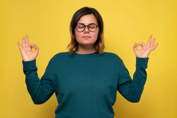 Jeune femme à lunettes gardant les yeux fermés tout en méditant, se sentant détendue — Photo