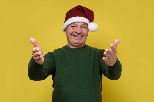 Homme âgé avec chapeau de Noël regardant la caméra souriant avec les bras ouverts pour étreindre. — Photo