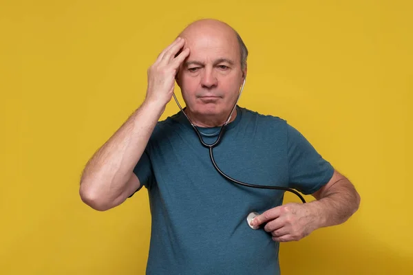 Worried senior man applying stethoscope to himself listening to his heart. — Stock Photo, Image