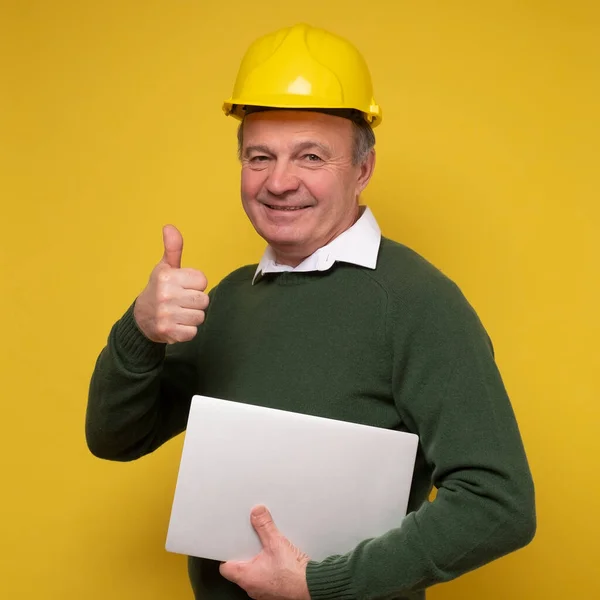 Hombre mayor con un sombrero duro especial que trabaja usando el ordenador portátil que aprueba mostrar el pulgar hacia arriba — Foto de Stock