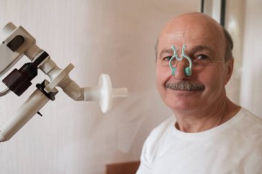 Senior man testing breathing function by spirometry clipart