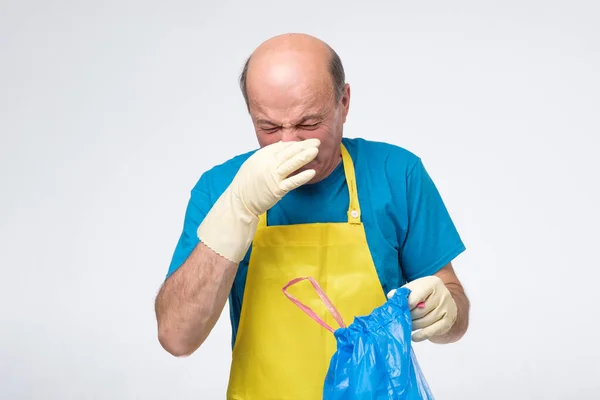 Caucásico hombre mayor sosteniendo una bolsa de basura cerrando la nariz debido al mal olor. —  Fotos de Stock