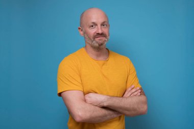 Elleri bağlı sakallı, kameraya kendinden emin bir şekilde bakan olgun bir adam.