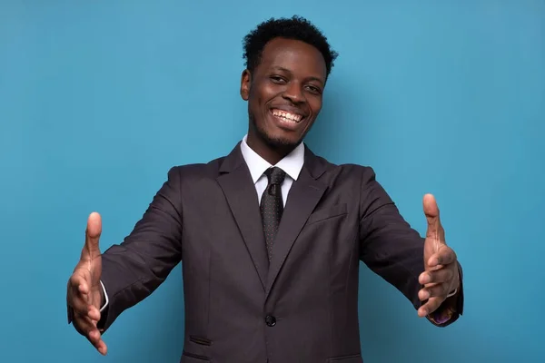 Jovem homem africano bonito sorrindo alegre com os braços abertos como boas-vindas amigáveis. — Fotografia de Stock