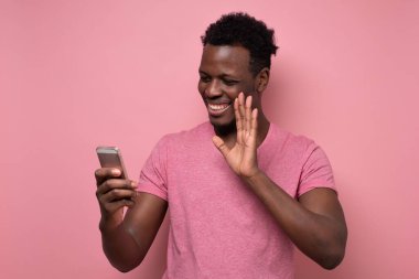 Afrikalı genç bir adam cep telefonunu elinde tutuyor, görüntülü konuşma sırasında el sallıyor..