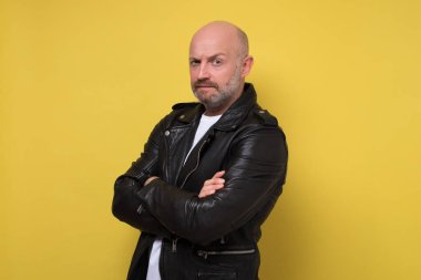 Ciddi bir orta yaşlı adam, kolları bağlı ve ciddi bir ifadesi var.