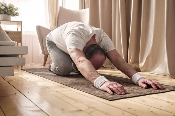 Hombre mayor activo haciendo la pose de niño mientras practica yoga en una estera —  Fotos de Stock