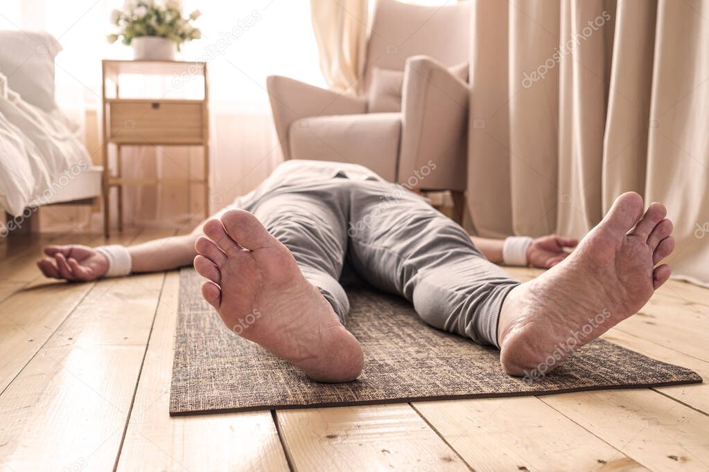 Caucasian man meditating on a wooden floor and lying in Shavasana pose