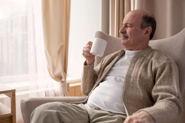 Portret van een ontspannen senior man zittend op de bank met warm drankje — Stockfoto