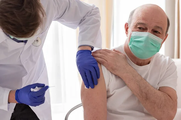 Médico vacunando a un paciente masculino mayor en casa. —  Fotos de Stock