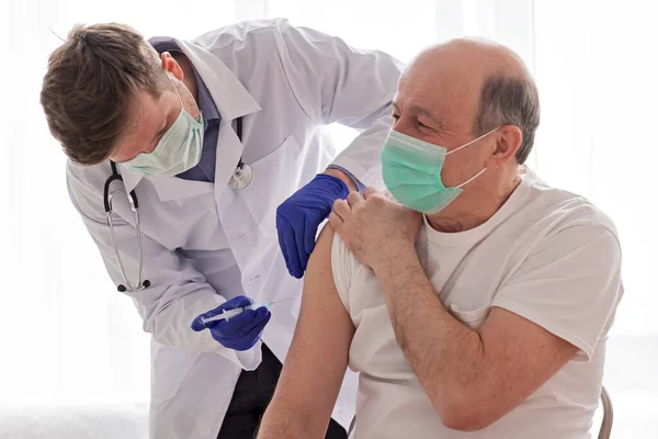 Arzt impft älteren männlichen Patienten zuhause. — Stockfoto