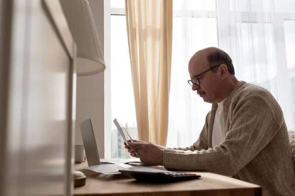 Senior man sitter med pappersarbete och använda miniräknare samtidigt räkna pengar — Stockfoto