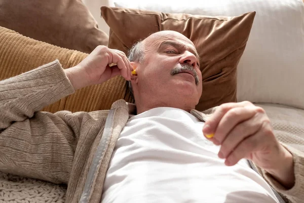Senior stresovaný muž drží žlutou špunt do uší se snaží spát s nespavostí — Stock fotografie