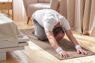 Paspasın üzerinde yoga yaparken çocuk pozu veren aktif kıdemli adam.