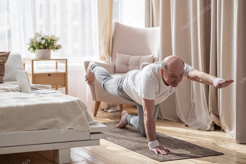 Senior caucasian men practices yoga asana chakravakasana, bird pose at home