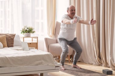 Üst düzey bir adam evde yoga yapıyor. Utkatasana 'da sandalye pozu veriyor.