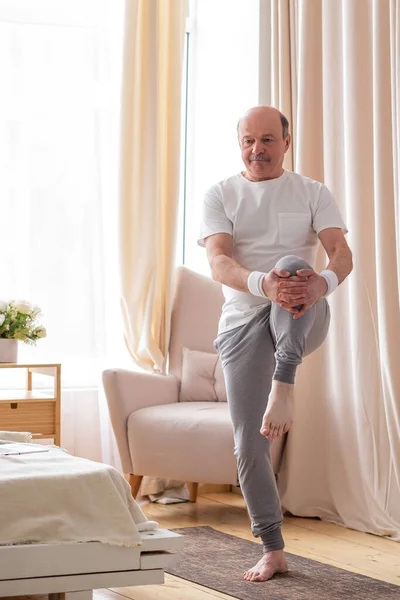 Esportista bonito sênior fazendo alongamento e equilibrando o exercício de ioga em casa — Fotografia de Stock