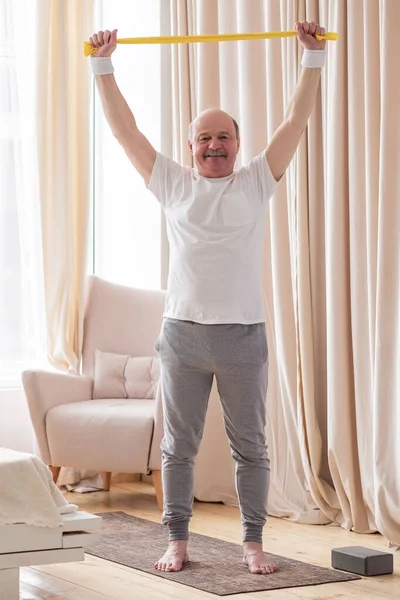 Senior man träning hemma tränar hemma med ett elastiskt band — Stockfoto