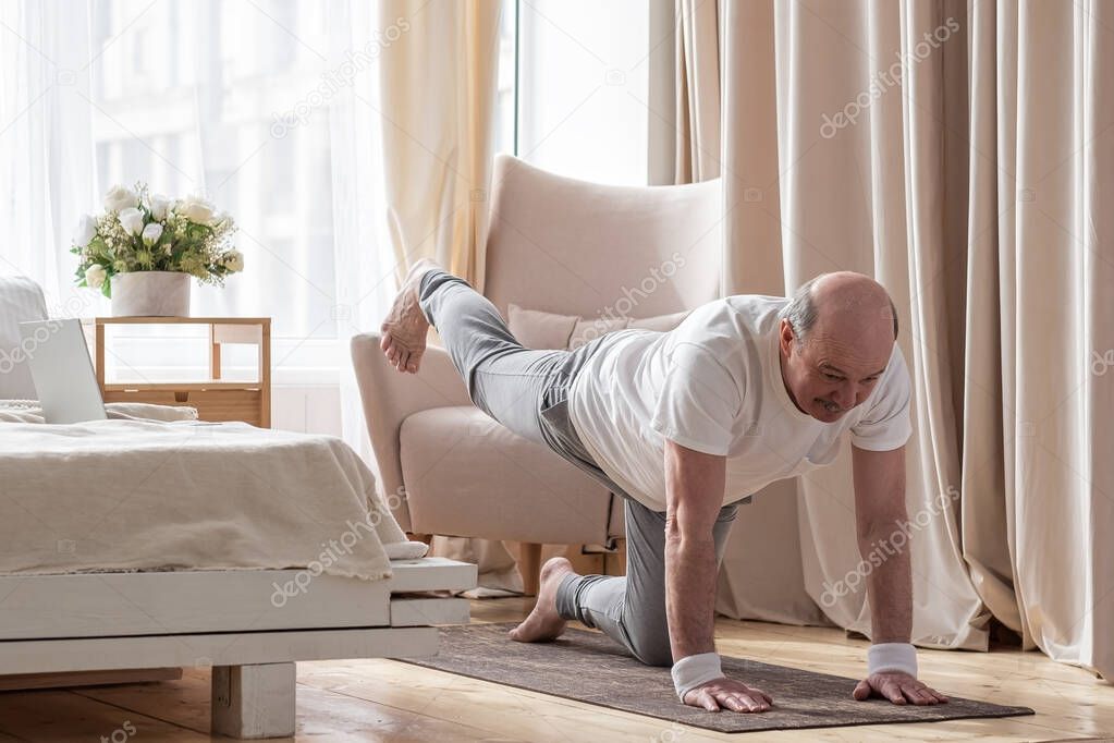 Senior caucasian men practices yoga asana chakravakasana, bird pose at home