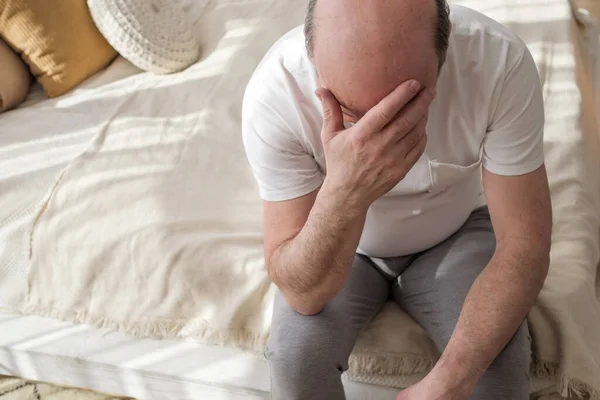 Sad caucasian man sitting on his bed with his head on his hand — Stock Photo, Image