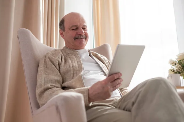 Старший мужчина на диване с планшетным компьютером дома — стоковое фото