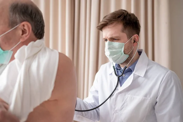 Лікар - самець Кавказу слухає, як старші чоловіки дихають стетоскопом. — стокове фото