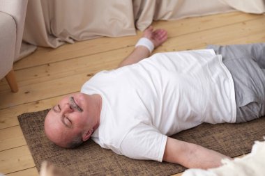 Kıdemli adam oturma odasının ahşap zemininde meditasyon yapıyor ve Shavasana 'da yatıyor.
