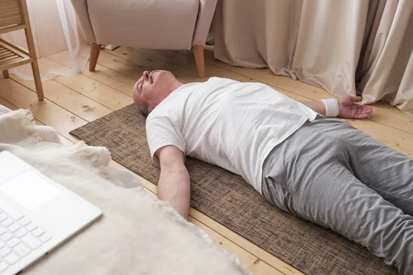 Uomo anziano meditando su un pavimento in legno di soggiorno e sdraiato a Shavasana — Foto Stock