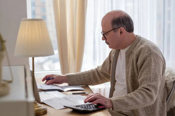 Senior man sitter med pappersarbete och använda miniräknare samtidigt räkna pengar — Stockfoto