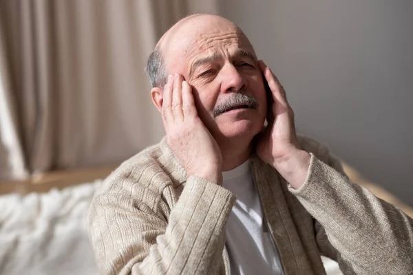 Oude man voelt pijn in zijn slaap alleen thuis zitten. — Stockfoto