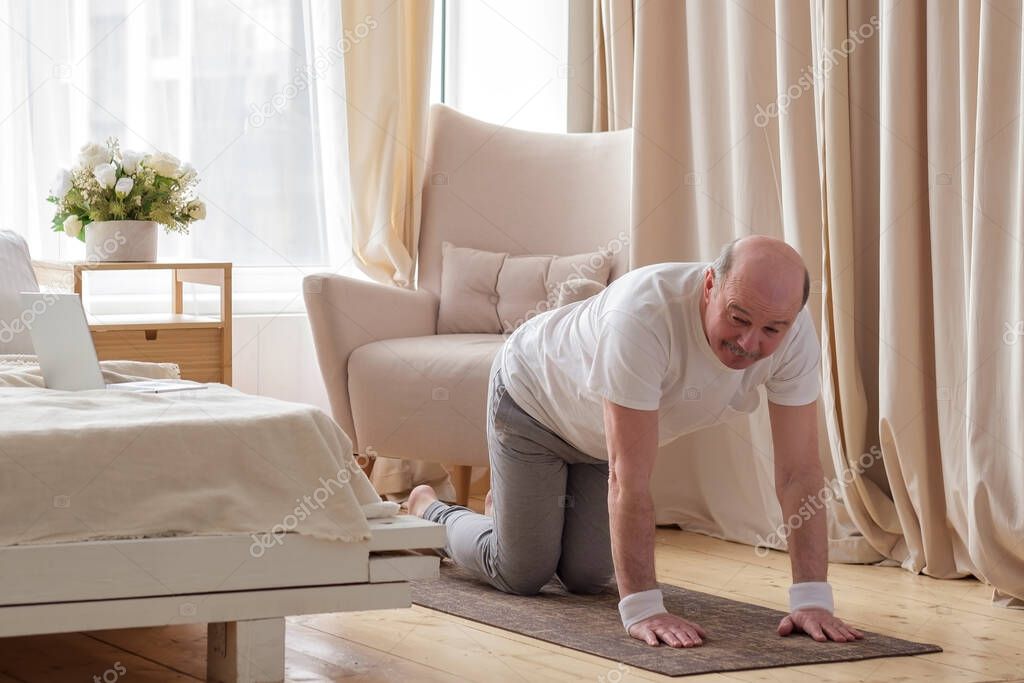 Senior caucasian men practices yoga asana chakravakasana, bird pose at home