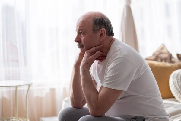 Triste hombre mayor con la cabeza en las manos sentado en la cama en casa —  Fotos de Stock