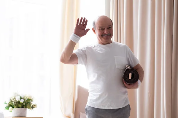 Hombre mayor sosteniendo esterilla de yoga renunciando a saludar feliz y sonriente —  Fotos de Stock