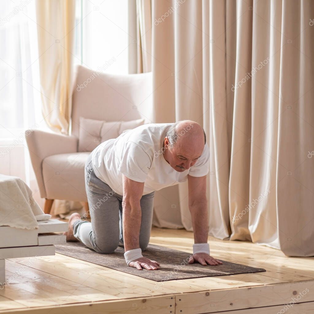 Senior man practices yoga asana chakravakasana, bird pose at home