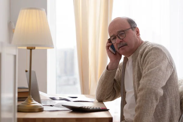 Старший говорит по телефону сидя за столом дома — стоковое фото