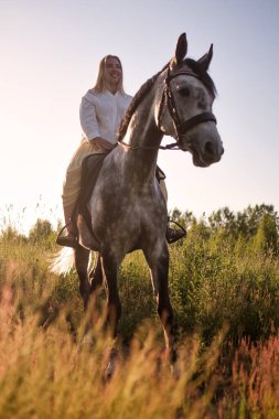 Genç sarışın kadın atıyla yürüyor.