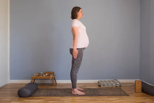 Hamile bir kadın yoga yapıyor, pilates yapıyor, iribaş duruyor, dağ pozu veriyor. — Stok fotoğraf