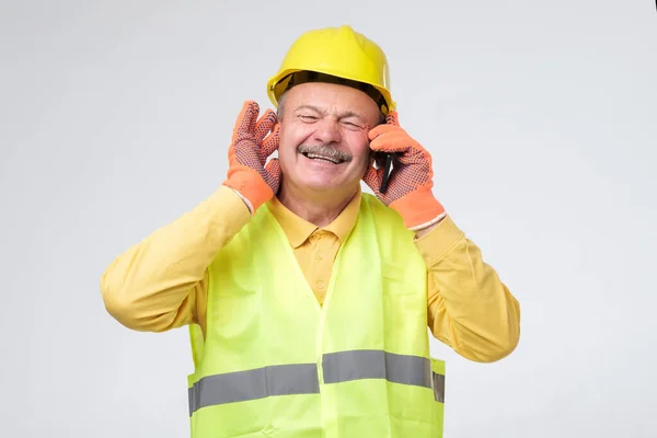 Trabajador con cascos de seguridad cierra sus otros oídos mientras habla por teléfono móvil — Foto de Stock