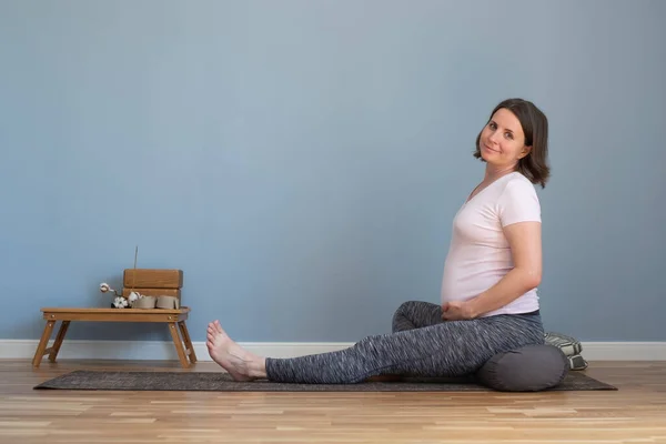 Hamile kadın yoga minderinde oturmuş kameraya bakıp gülümsüyor.. — Stok fotoğraf
