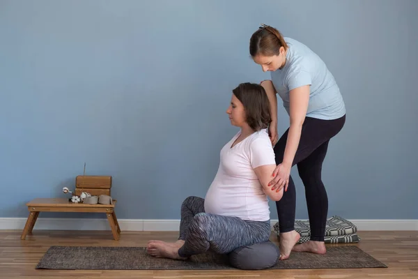 Antrenör, hamile bir kadının omuzları için yoga yapmasına yardım ediyor. — Stok fotoğraf