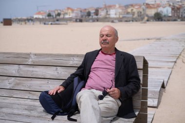 Yaşlı bir adam sahilde bir bankta oturuyor, dinleniyor ve güneşleniyor. Yüksek kalite fotoğraf