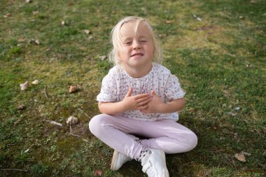 4 year old girl sitting on the grass making a painful grimace does not want to go anywhere. High quality photo