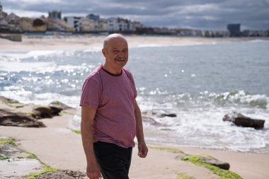 Bıyıklı yaşlı bir adam deniz kenarında yürüyor ve güneşli bir tatil gününün tadını çıkarıyor. Yüksek kalite fotoğraf