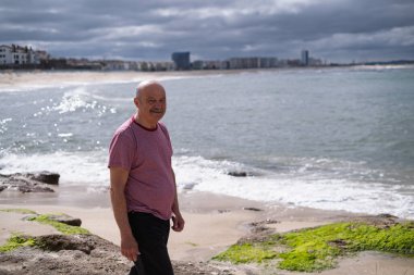 Bıyıklı yaşlı bir adam deniz kenarında yürüyor ve güneşli bir tatil gününün tadını çıkarıyor. Yüksek kalite fotoğraf