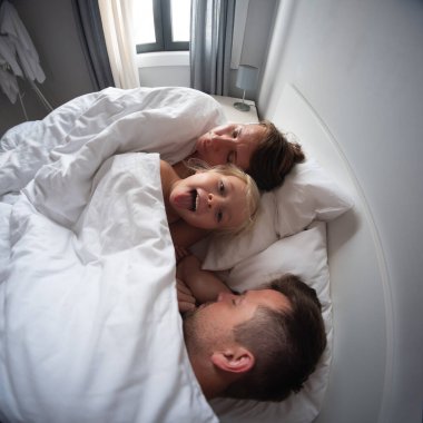 Oyuncu 4 yaşındaki kız, anne babasıyla yatakta eğleniyor, sabahları uyumalarına izin vermiyor. Yüksek kalite fotoğraf