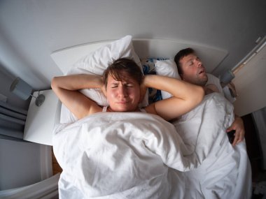 Karısı kulaklarını kapatırken, gürültüden uyuyamayan bir adam yatakta yüksek sesle horluyor. Yüksek kalite fotoğraf