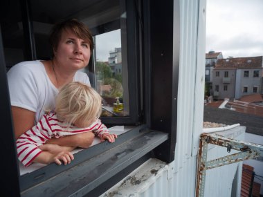 Genç anne ve çocuğu dışarı bakıyor. Yağmur yağıyor mu diye kontrol ediyor. Yüksek kalite fotoğraf