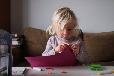 Küçük kız evde zanaat yapıyor, kağıt kesiyor ve masada resim çiziyor. Yüksek kalite fotoğraf