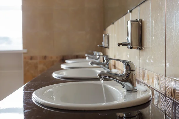 In einer öffentlichen Toilette fließt Wasser aus dem Wasserhahn. Niemand hier. — Stockfoto