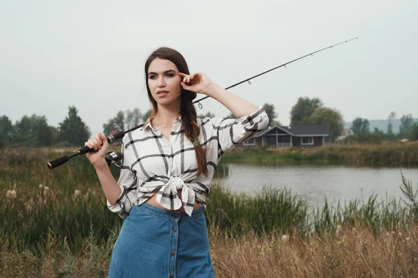 Country lady standing against pond on ranch with fish-rod — Stock Photo, Image